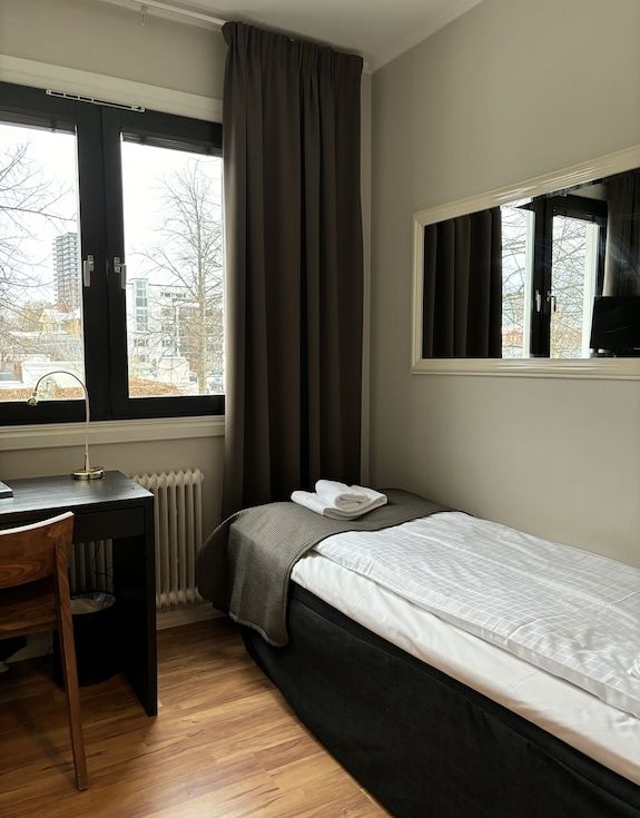 Litet enkelrum med säng, skrivbord och utsikt över stadsmiljö i Växjö.